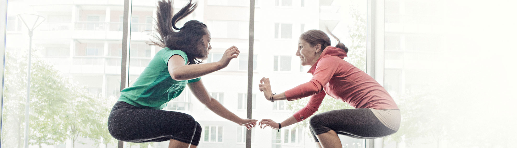 Två träningsklädda kvinnor hoppar upp mittemot varandra.