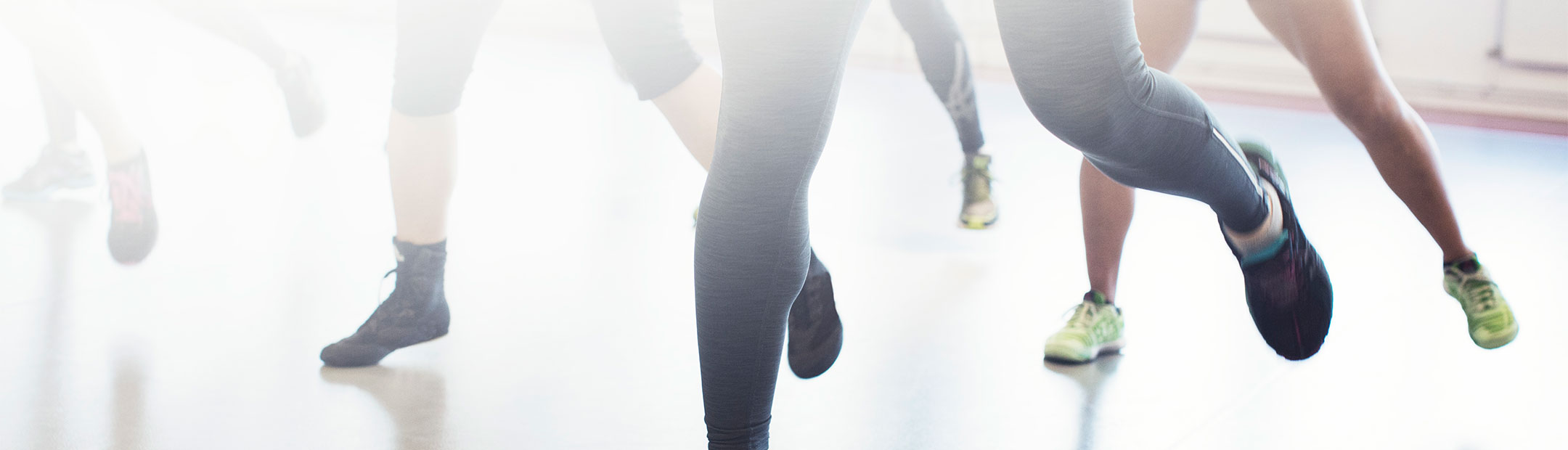 Närbild på en grupp träningsklädda människors fötter som är i rörelse i en träningssal på Friskis&Svettis.