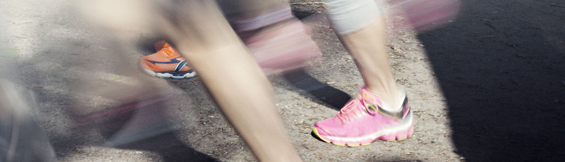 Närbild på rosa och orangea löparskor som snabbt springer förbi på grusväg.
