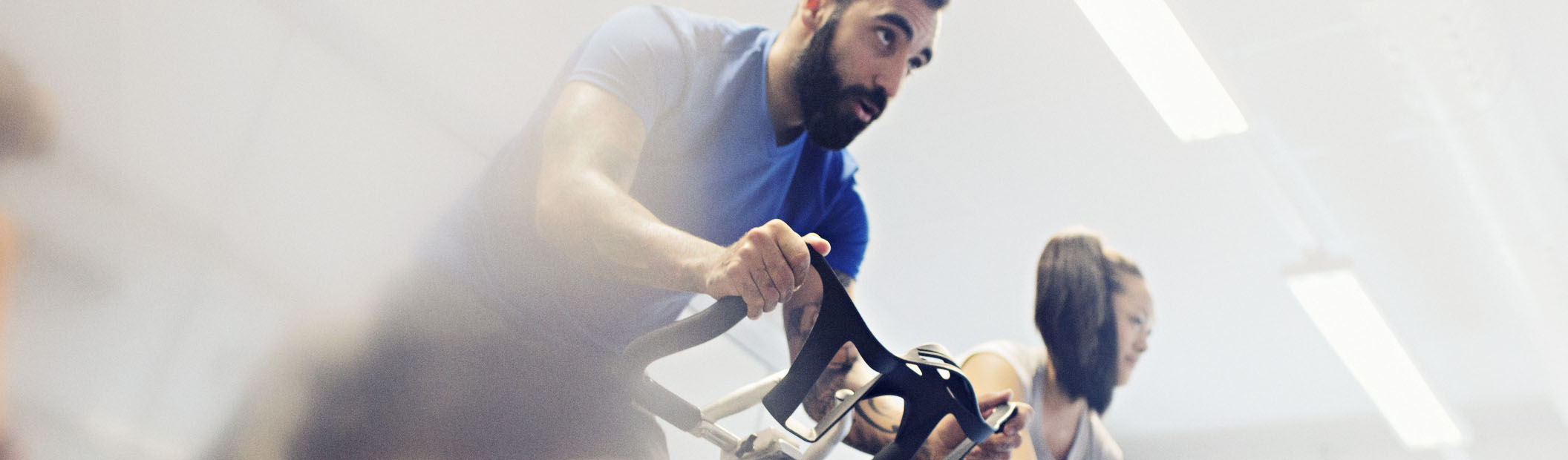 En man i blå t-shirt står upp och cyklar på en spinningcykel i en spinsal på Friskis&Svettis.