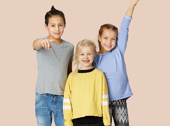 Tre barn i 7-9 års åldern som ler, skrattar, sträcker ut och upp armarna till rörelse