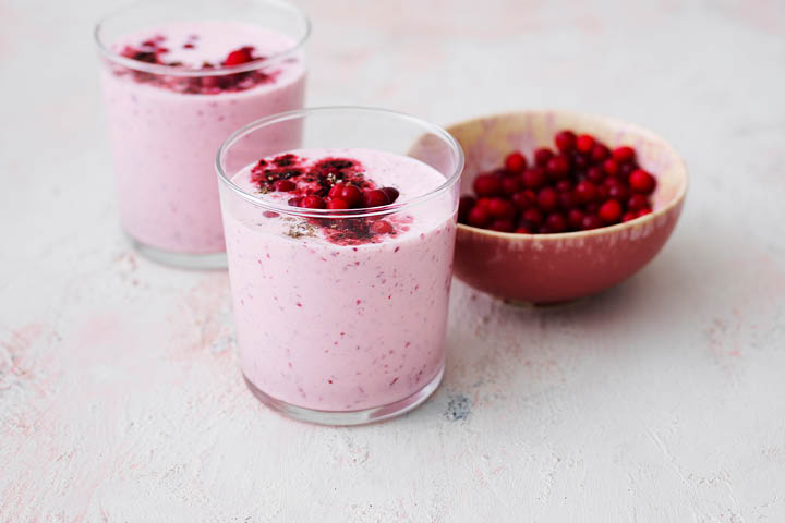 Två glas fyllda med vackert rosa smoothie och bär på toppen. Bredvid en skål med lingon.